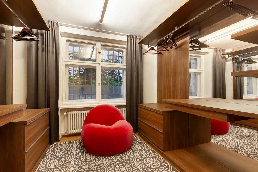 Ankleidezimmer mit Holzschränken, Teppich und rotem Sitzsack vor einem Fenster.