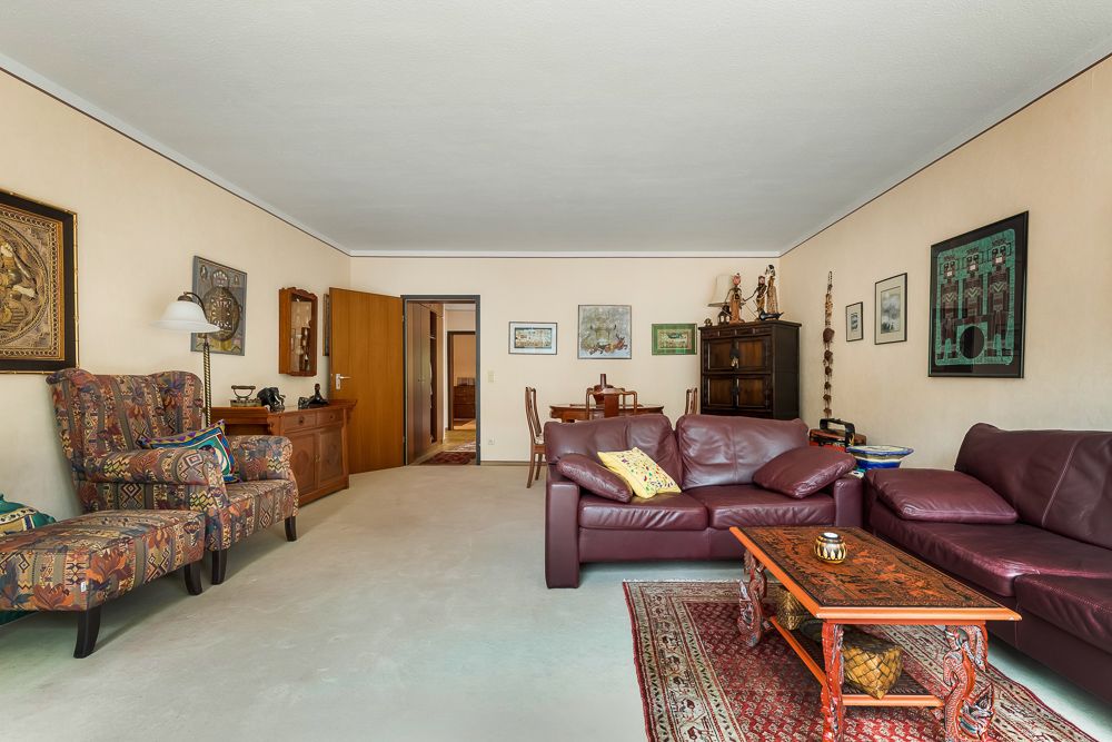 Wohnzimmer mit Ledersofa, gemusterten Sesseln, Teppich und Holztisch, an den Wänden hängen Bilder.