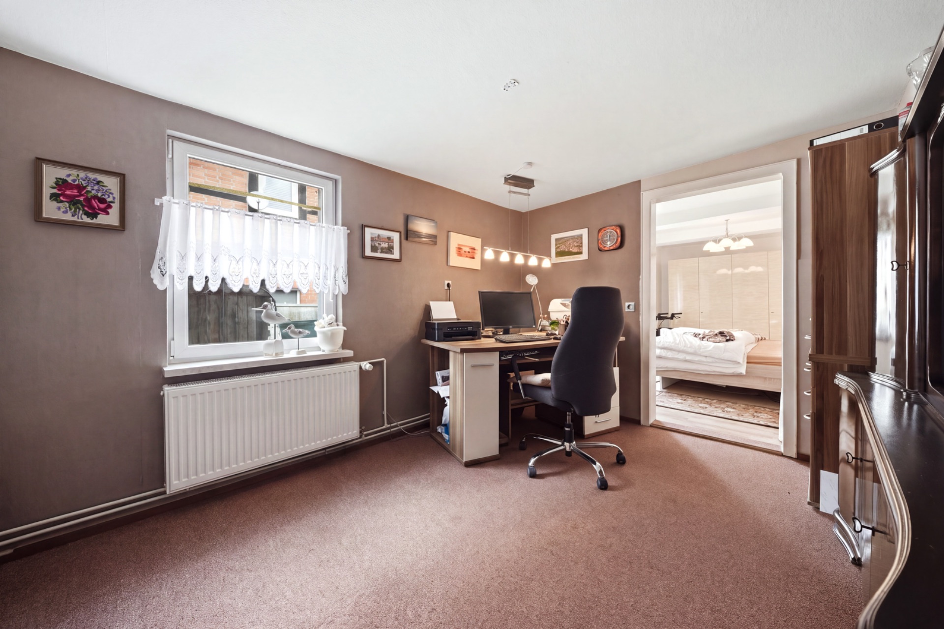 Arbeitszimmer mit Schreibtisch, Stuhl, Fenster und Blick in ein Schlafzimmer.