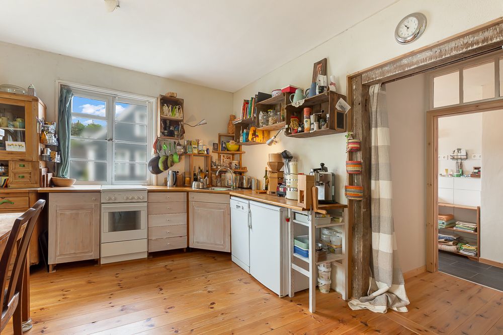 Helle Küche mit Holzfußboden, offenem Regal, Herd, Spüle und Küchenutensilien.