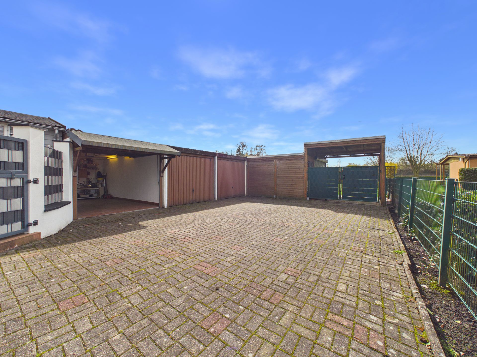 Gepflasterter Hof mit mehreren Garagen und Carport, umgeben von grünem Metallzaun.