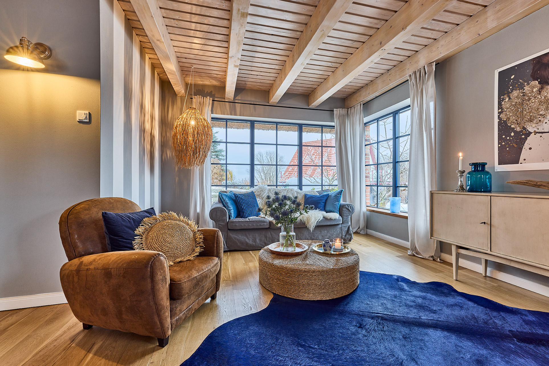 Helles Wohnzimmer mit Ledersessel, Sofa, Holzbalkendecke und großen Fenstern.