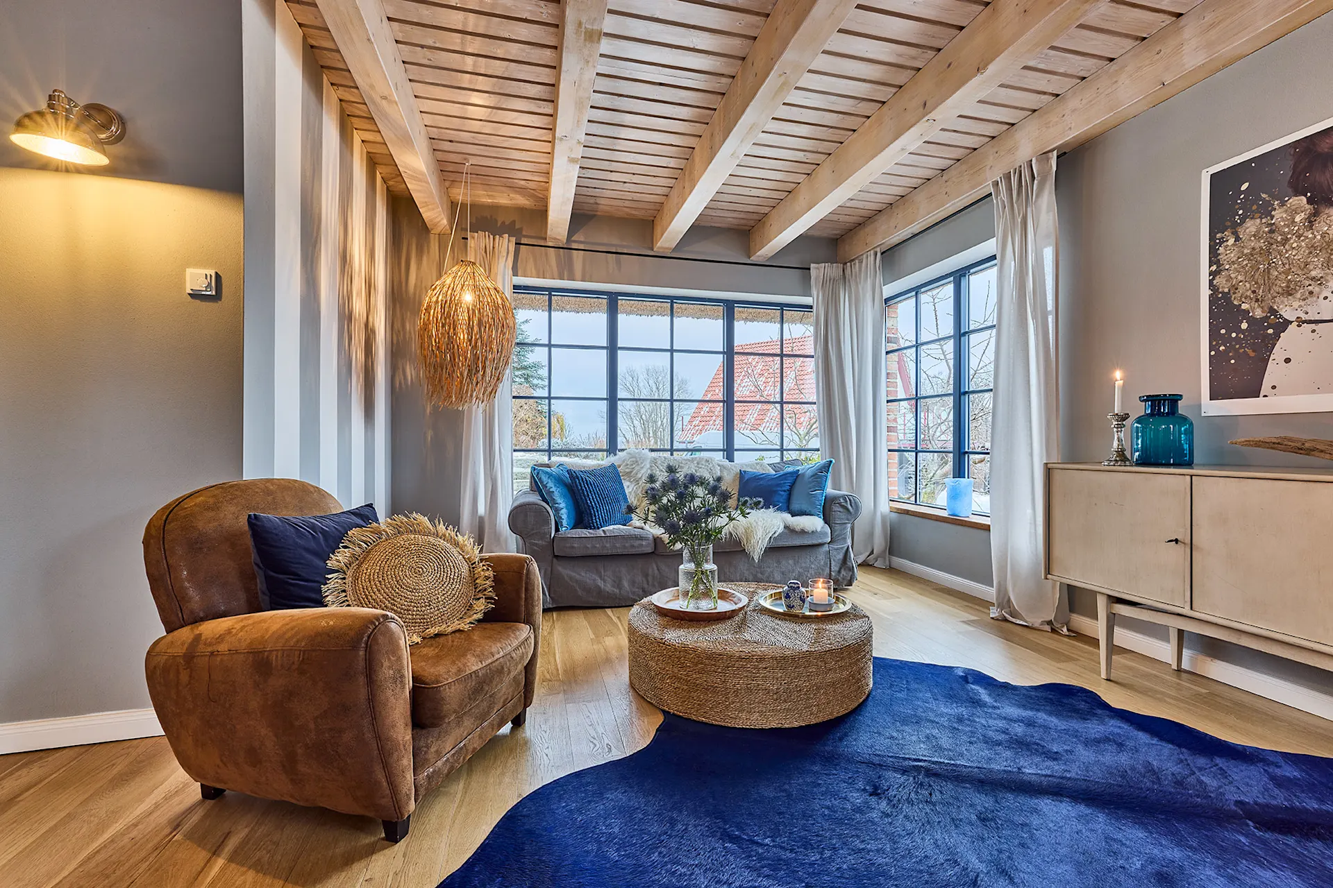 Helles Wohnzimmer mit Ledersessel, Sofa, Holzbalkendecke und großen Fenstern.