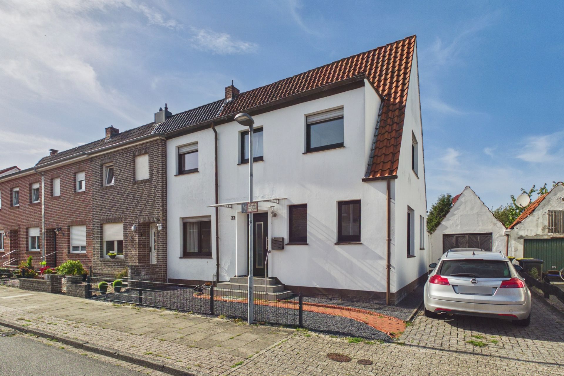 Zweistöckiges Reihenhaus mit weißer Fassade, rotem Dach und geparktem Auto vor dem Haus.