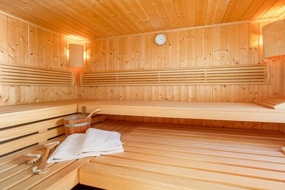 Holzsauna mit Bänken, Eimer, zwei Handtüchern und einer Uhr an der Wand.