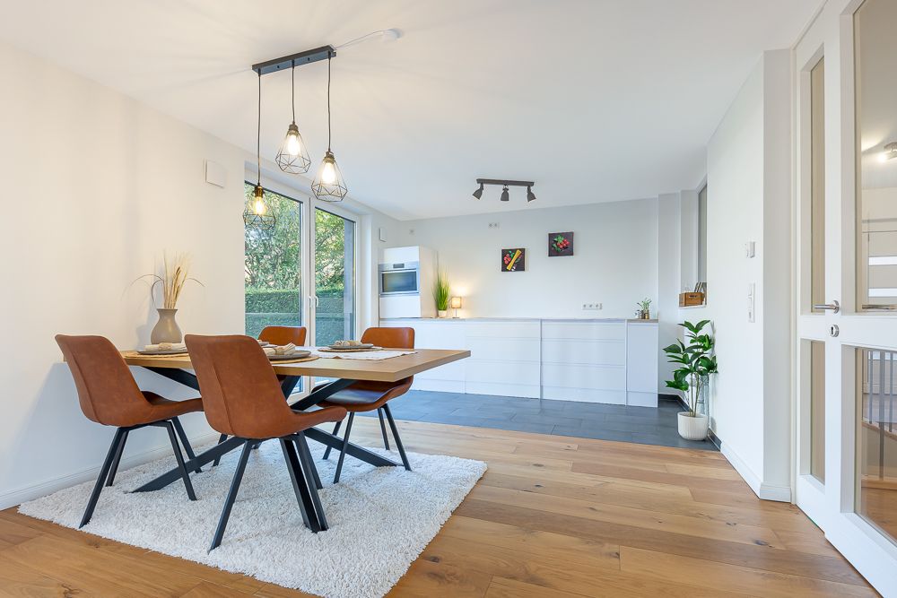 Modernes Esszimmer mit Holztisch, vier Stühlen und offener Küche im Hintergrund.