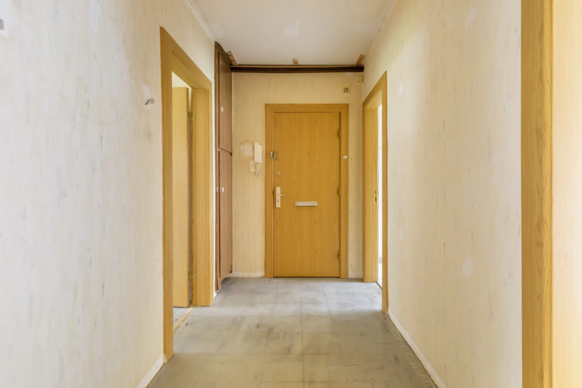 Heller Flur mit Holztüren und einer Eingangstür am Ende, Wände und Boden sind schlicht.