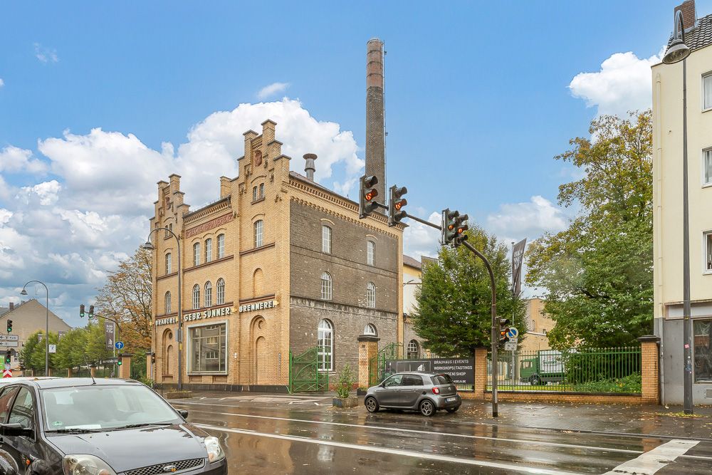 Altes Backsteingebäude mit Turm und Schornstein an einer nassen Straßenkreuzung.