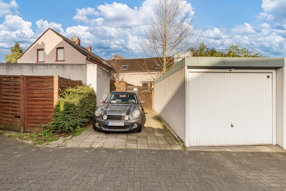 Auto parkt auf Auffahrt neben einer geschlossenen Garage vor einem Wohnhaus.