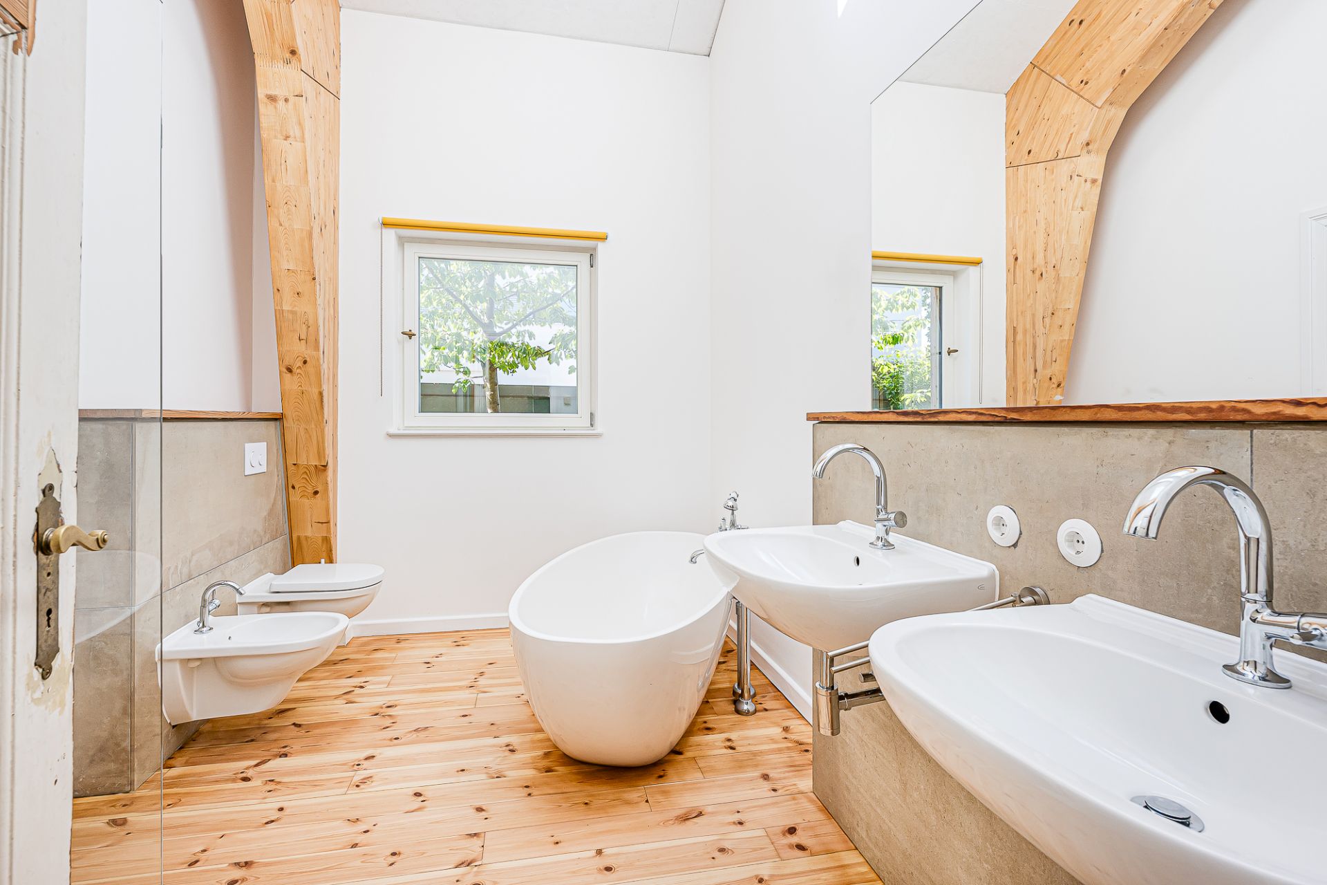 Modernes Badezimmer mit freistehender Badewanne, zwei Waschbecken und Holzfußboden.