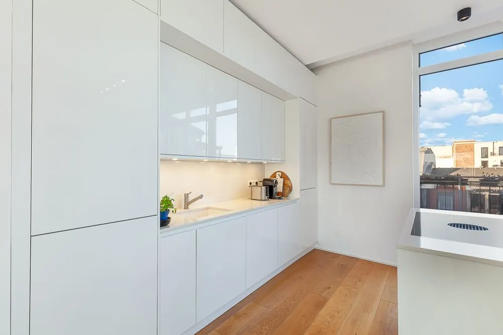 Moderne weiße Küche mit Holzfußboden, großen Fenstern und minimalistischem Design.