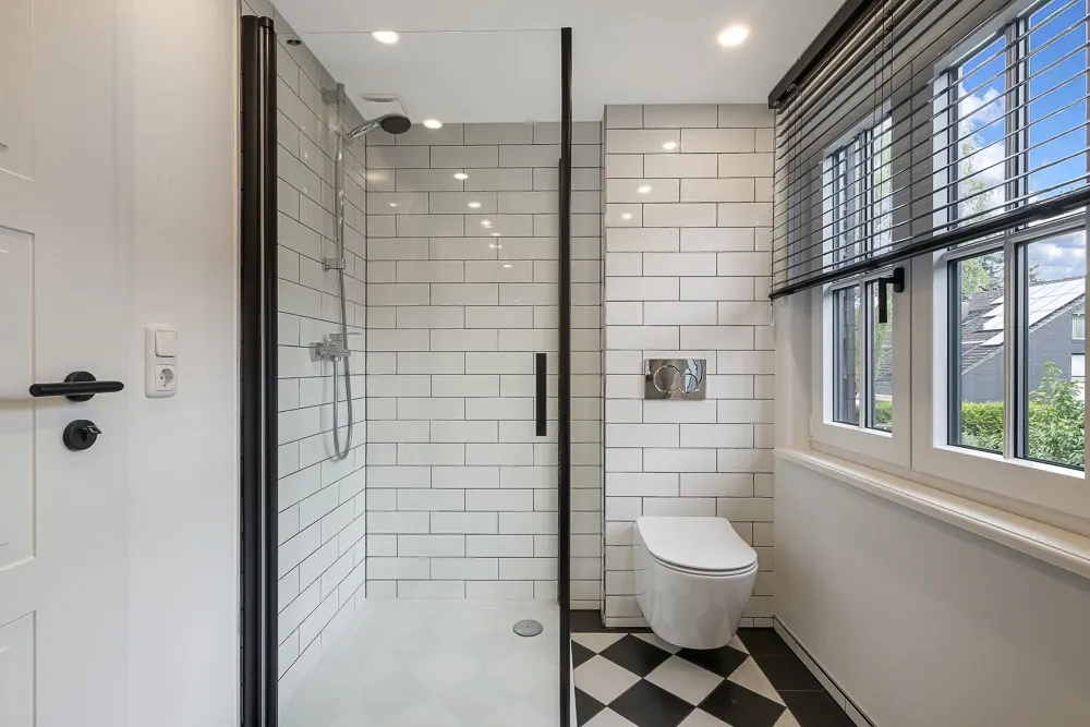 Modernes Bad mit bodentiefer Dusche, Wandtoilette und großem Fenster mit Jalousien.