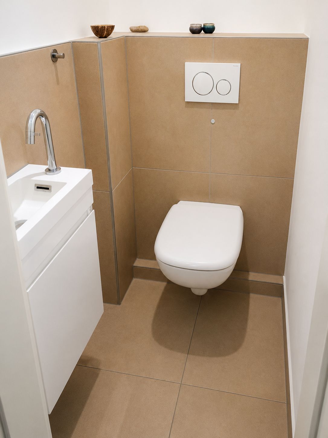Modernes kleines WC mit Hänge-Toilette, kleinem Waschbecken und hellbraunen Fliesen.