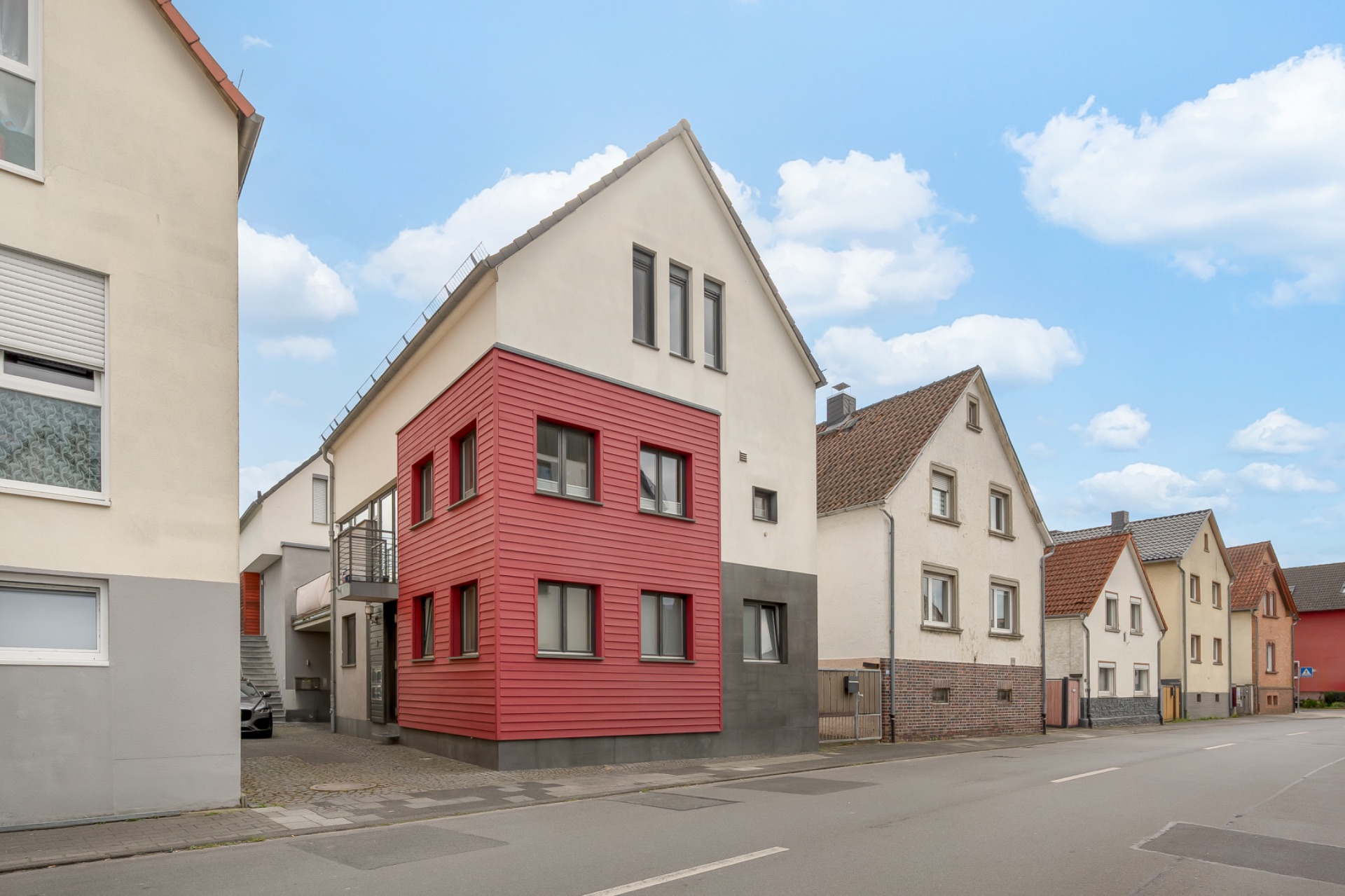 Wohnhaus mit rotem Anbau und mehreren Fenstern an einer ruhigen Straße.