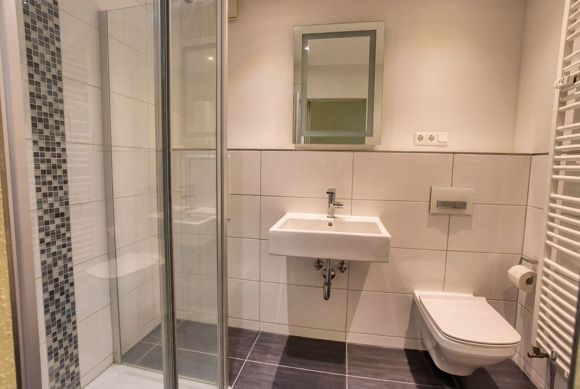 Modernes Bad mit Dusche, Waschbecken, Spiegel und wandhängender Toilette.