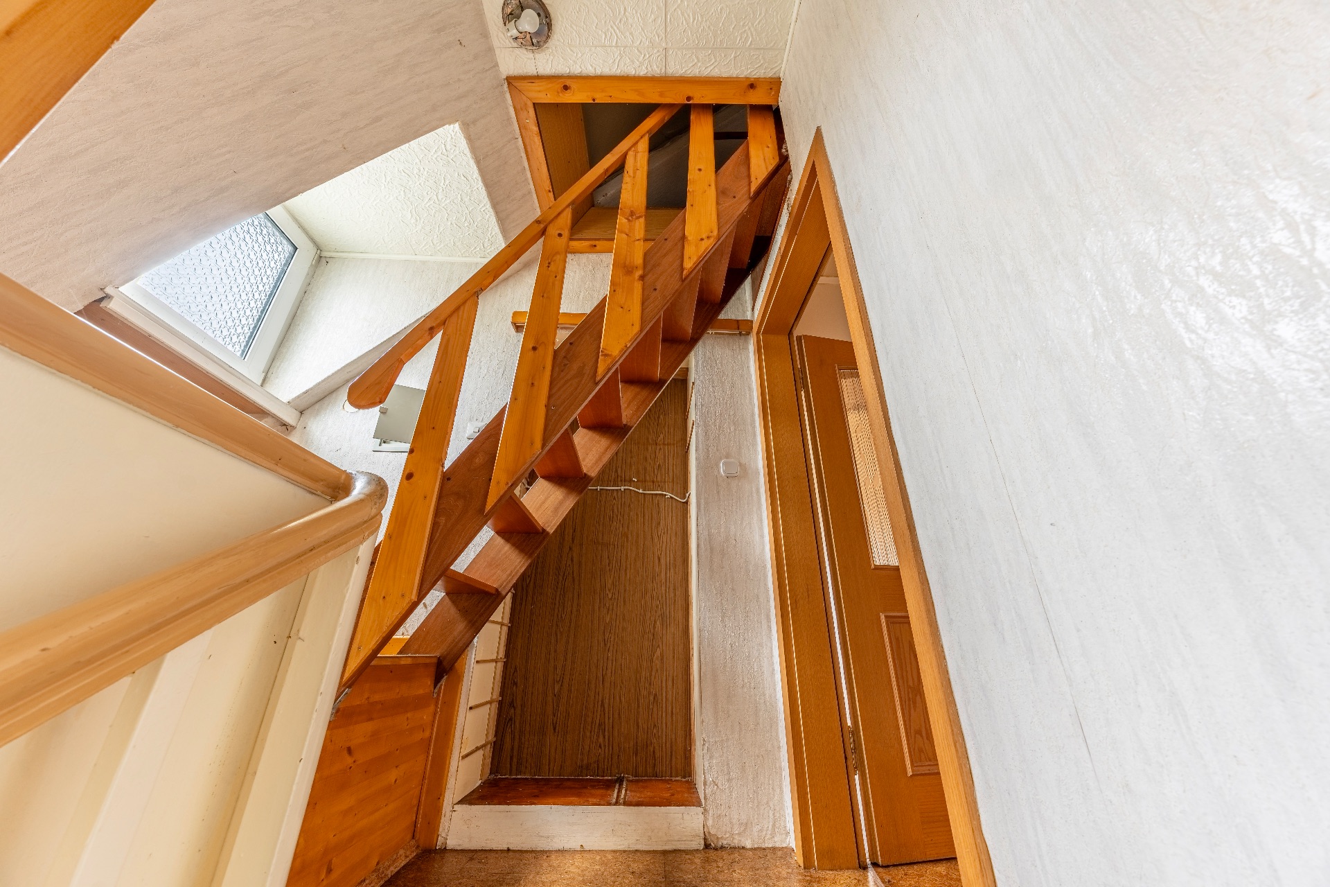 Holztreppe in einem Flur mit weiß gestrichenen Wänden und einem Fenster.