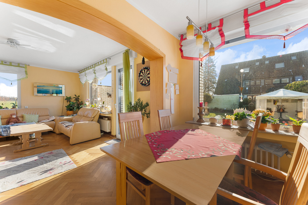 Helles Wohnzimmer mit Essecke, vielen Pflanzen, großen Fenstern und Blick in den Garten.