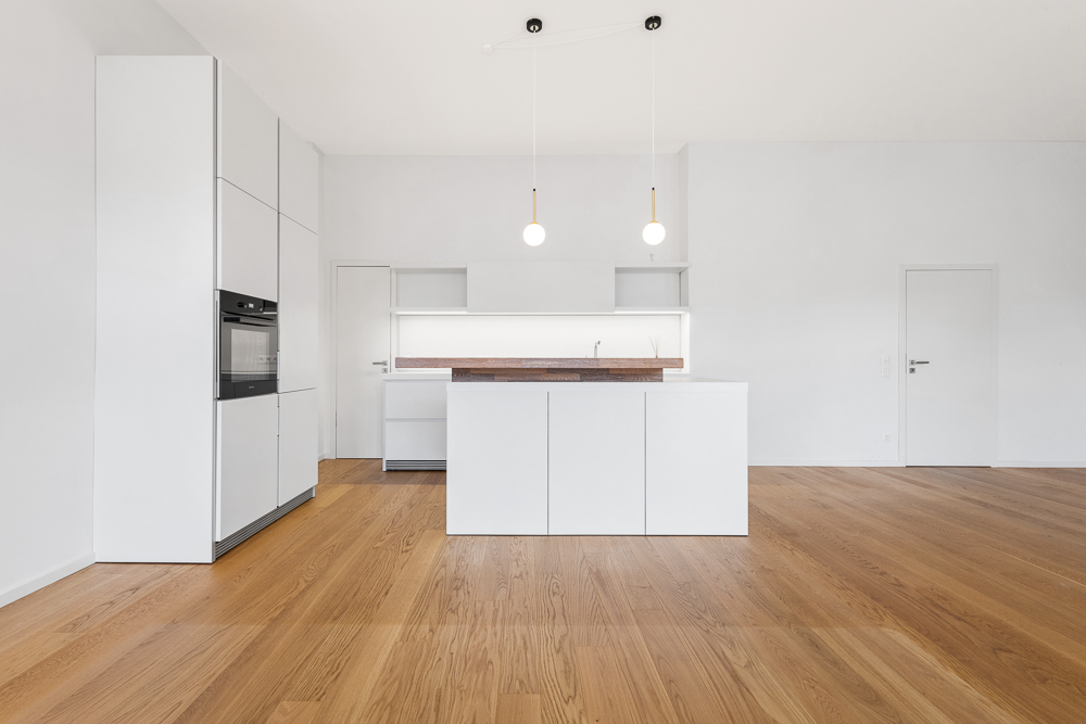 Moderne, weiße Küche mit Kochinsel und Holzfußboden in einem hellen Raum.