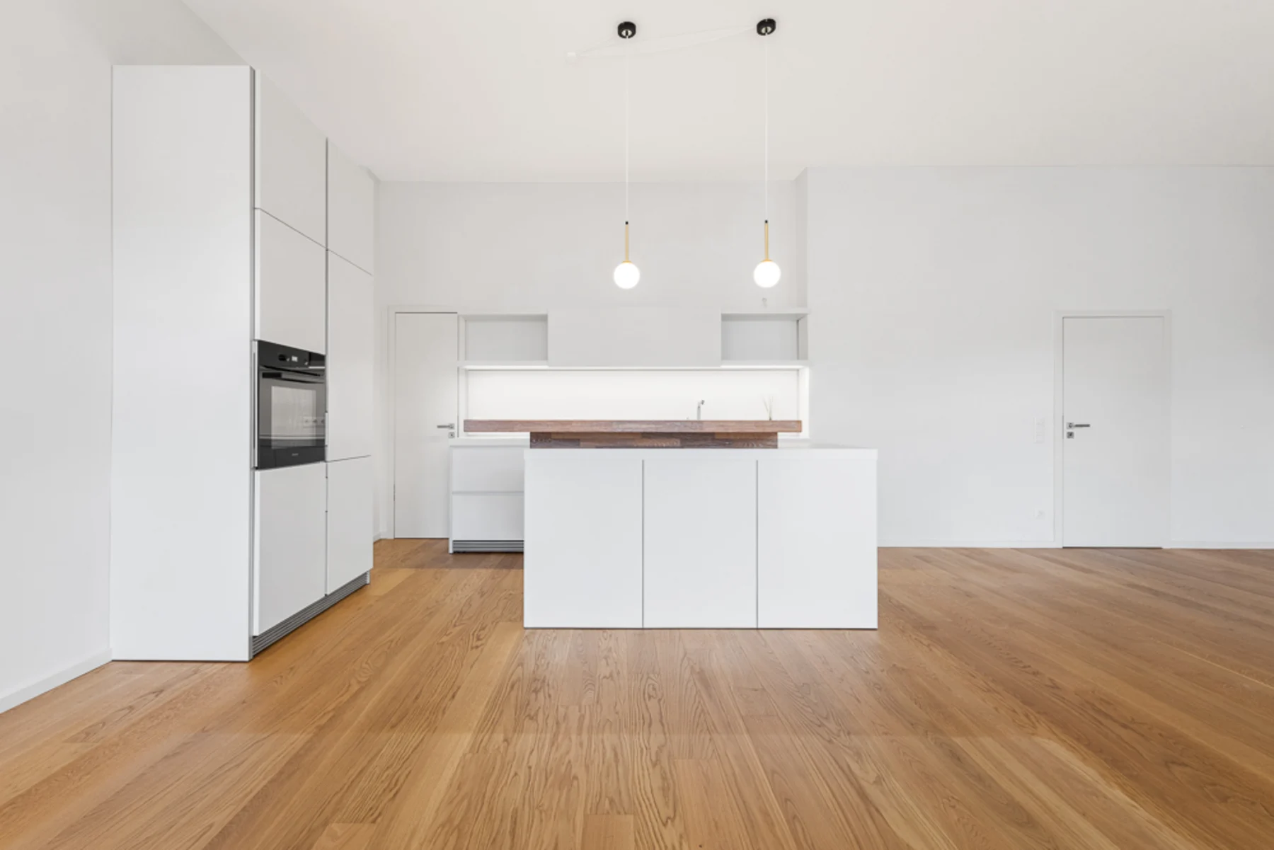 Moderne, weiße Küche mit Kochinsel und Holzfußboden in einem hellen Raum.