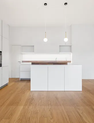 Moderne, weiße Küche mit Kochinsel und Holzfußboden in einem hellen Raum.