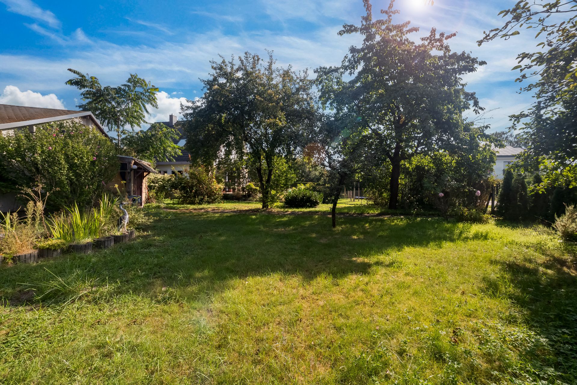 Grüner Garten mit Rasen, Bäumen und Sträuchern, daneben ein kleines Gartenhaus.