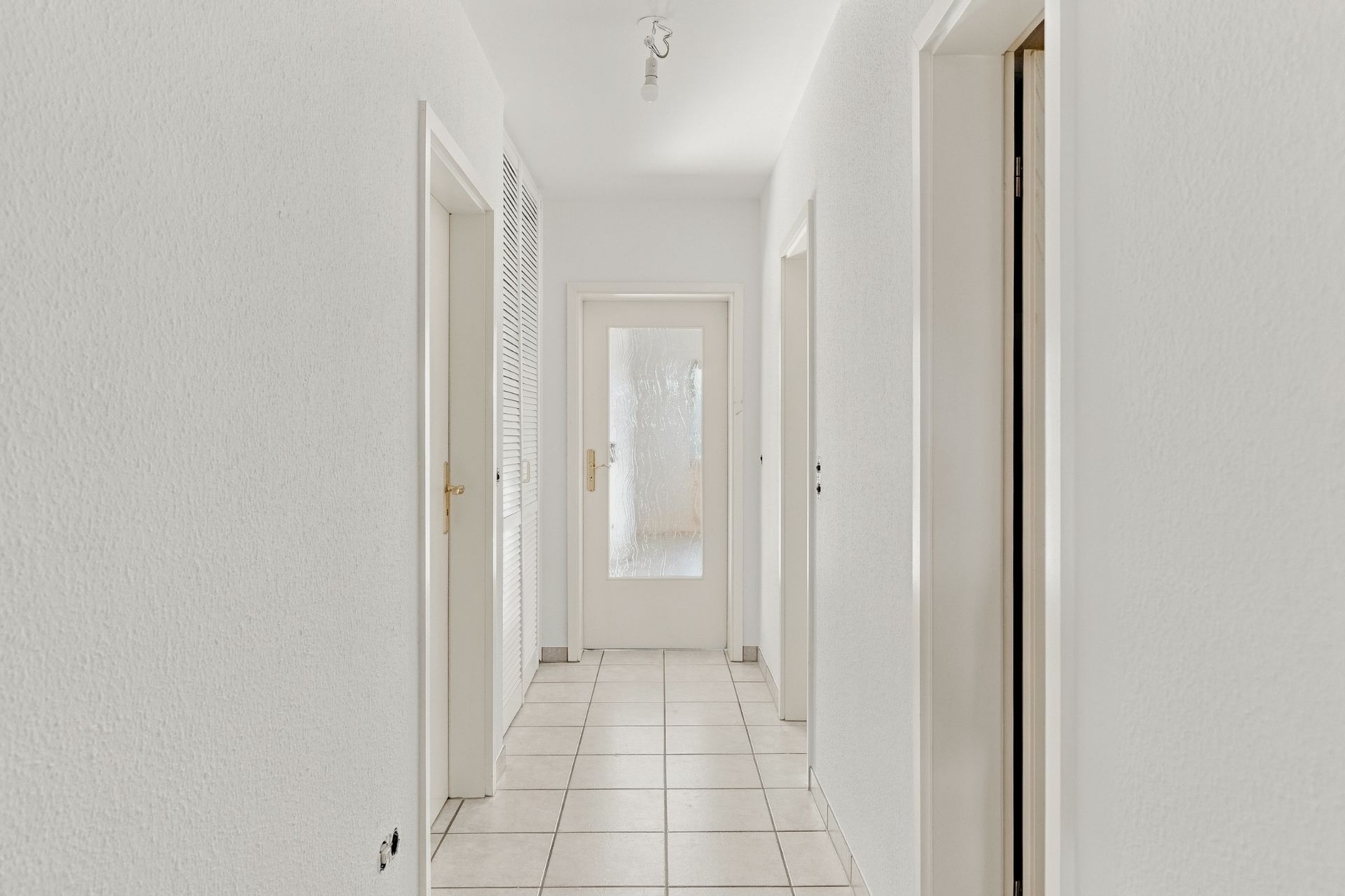 Heller Flur mit weißen Wänden, mehreren Türen und einer Glastür am Ende.