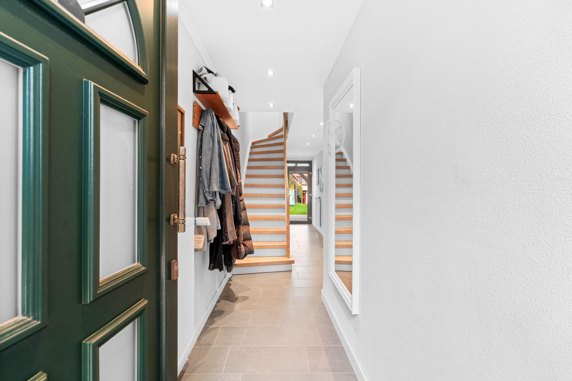 Heller Flur mit Spiegel, Garderobe und Treppe, die zu einer Tür im Hintergrund führt.