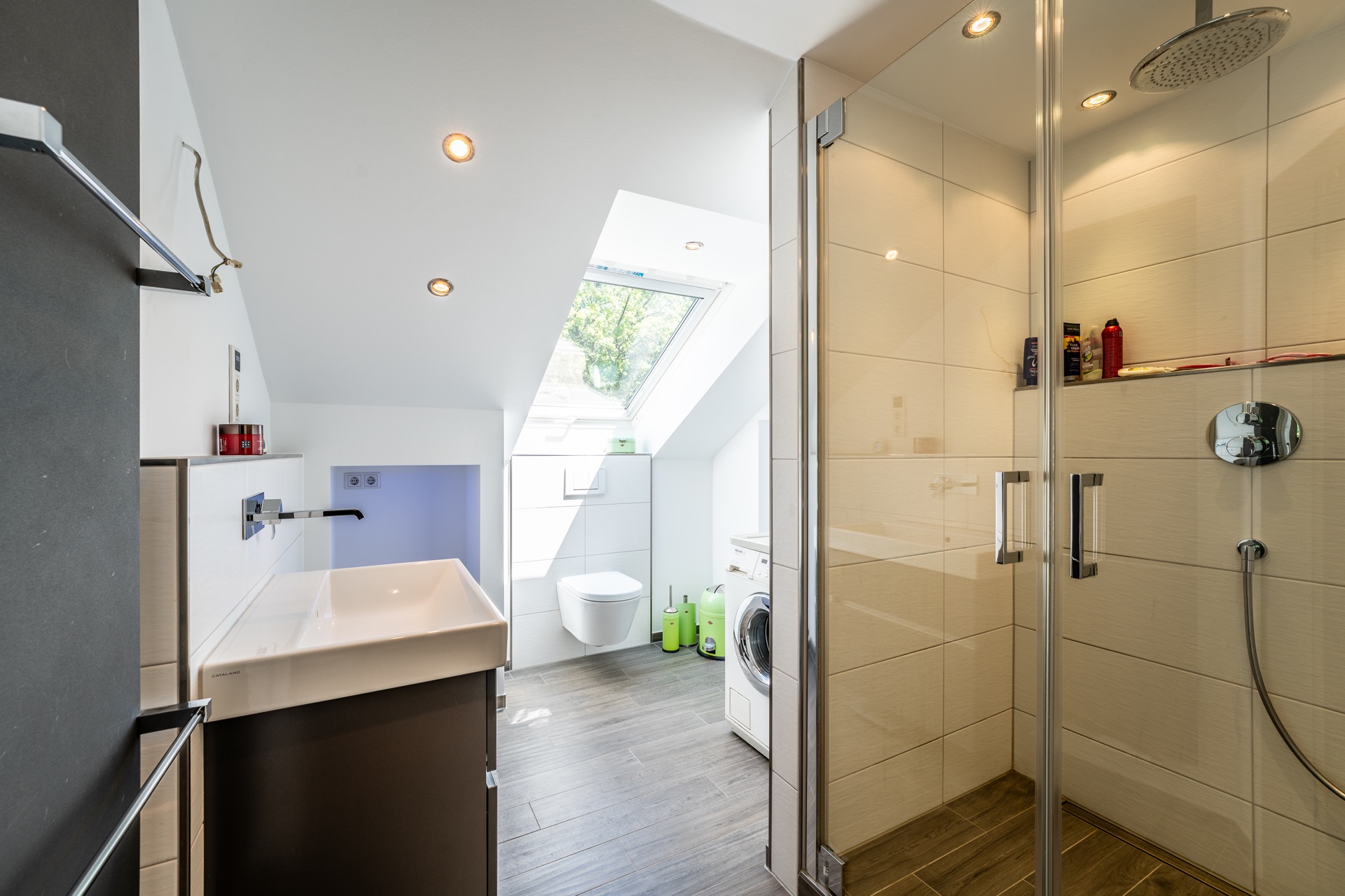 Modernes Badezimmer mit Dusche, Waschbecken, WC, Waschmaschine und Dachfenster.