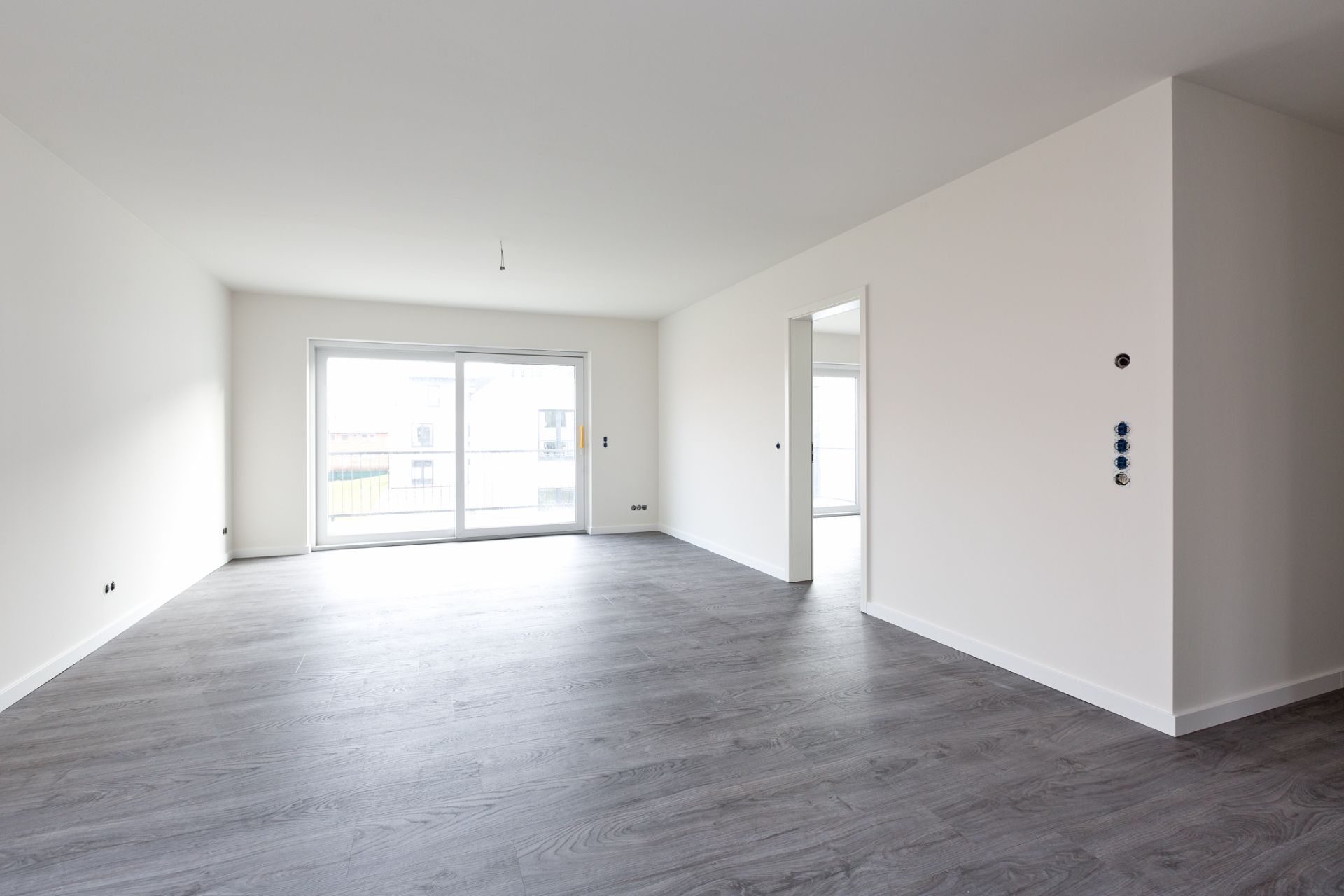 Heller, leerer Raum mit grauem Boden und großer Glas-Schiebetür zu einem Balkon.