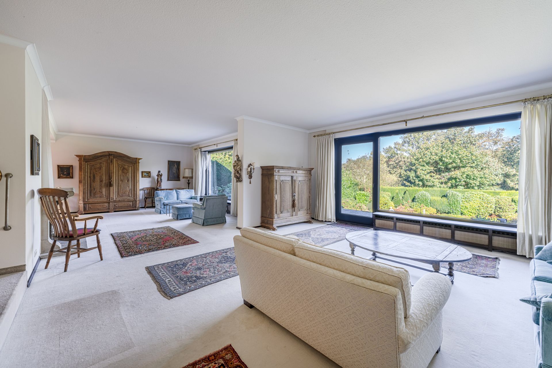 Großes Wohnzimmer mit Teppichen, Sesseln, Sofas und großem Fenster mit Blick auf den Garten.
