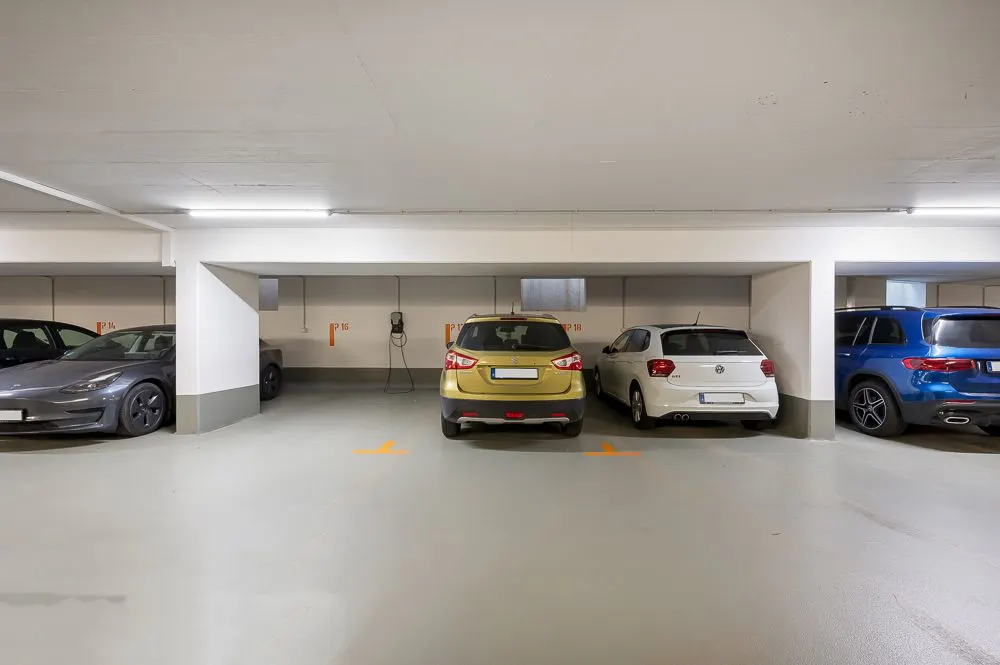Tiefgaragenstellplätze mit mehreren geparkten Autos und Ladestation an der Wand.
