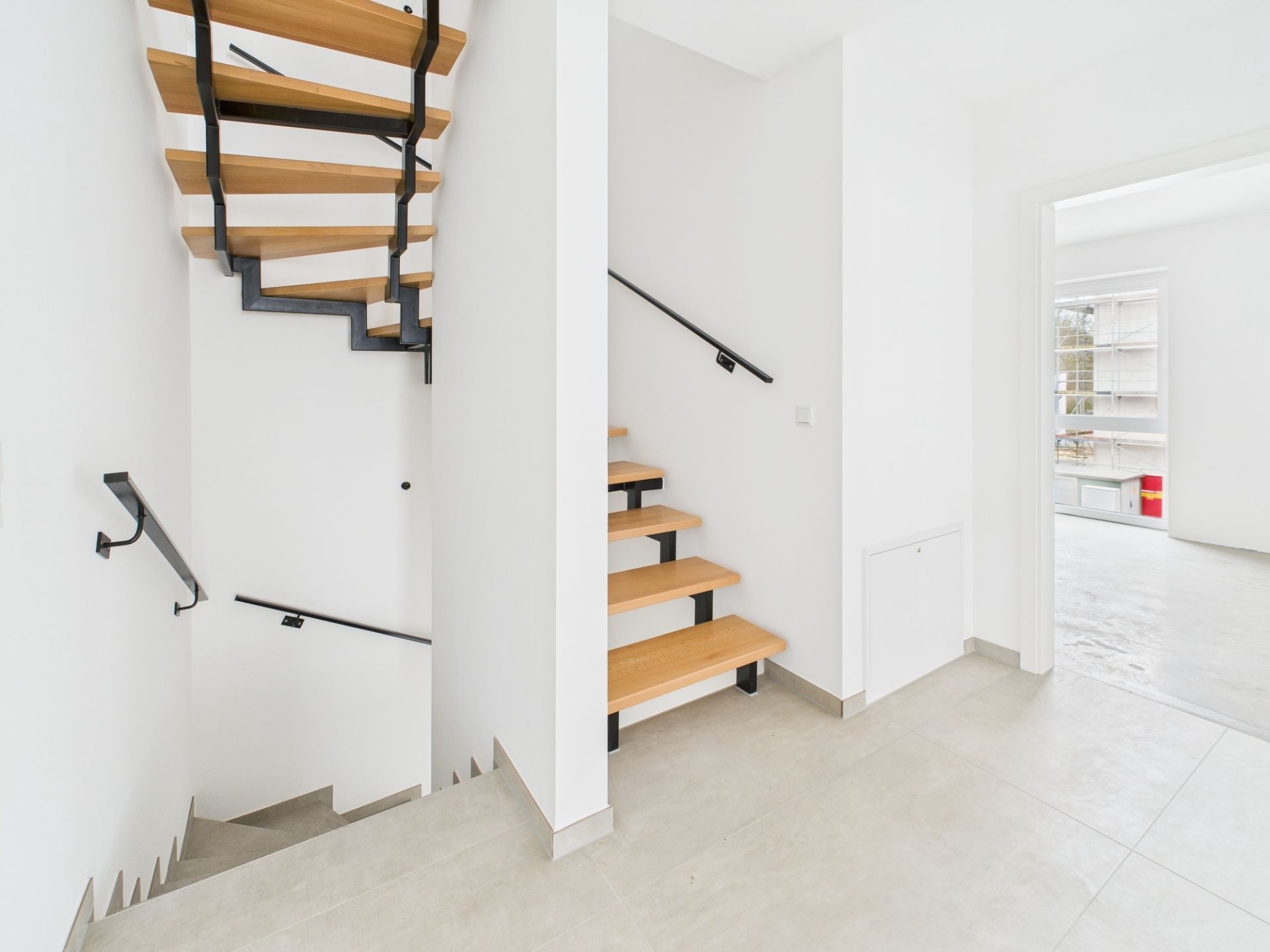 Heller Flur mit moderner Holztreppe und offenen Türen zu weiteren Zimmern.