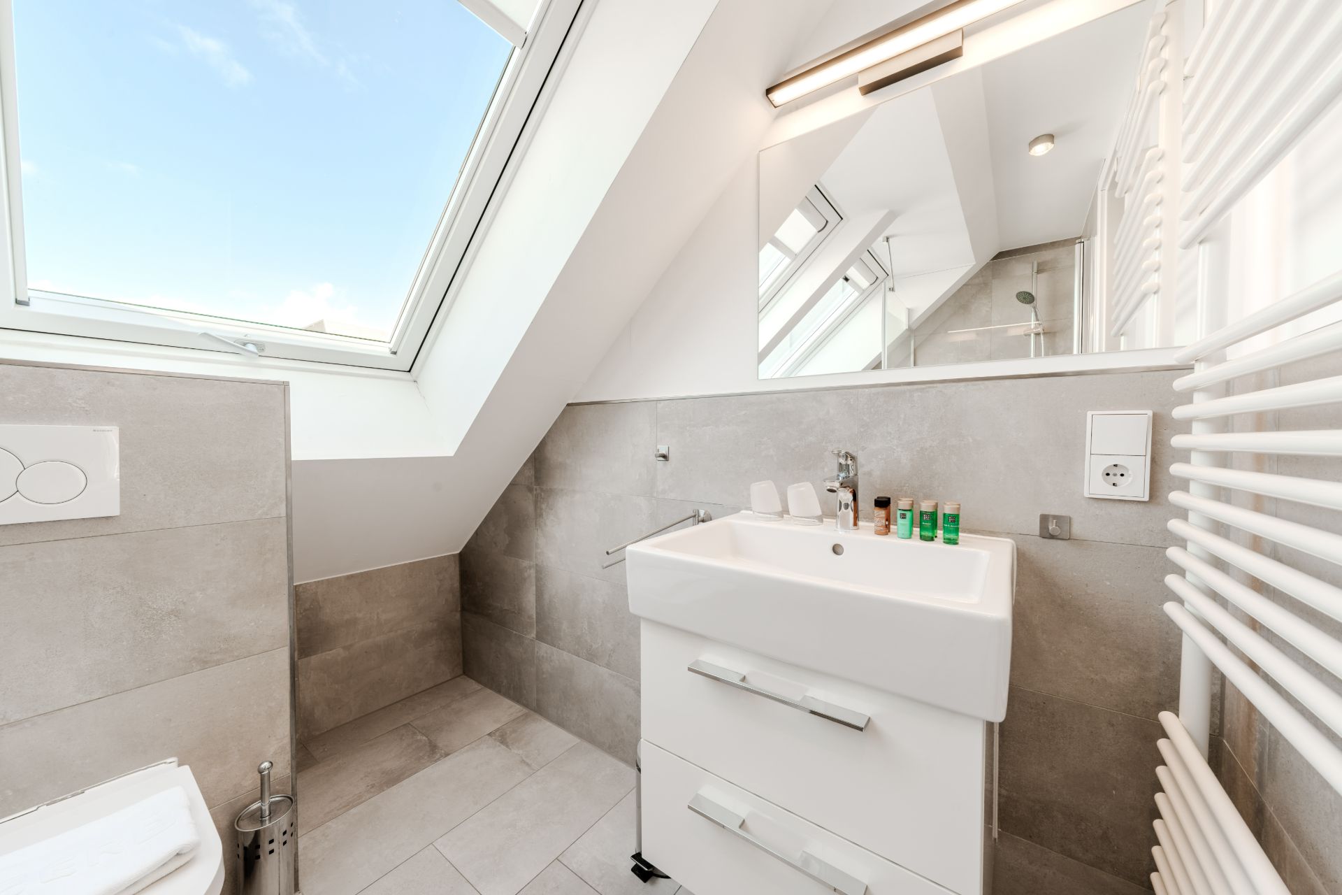 Modernes Badezimmer mit Dachfenster, Waschbecken, Spiegel und Handtuchheizkörper.