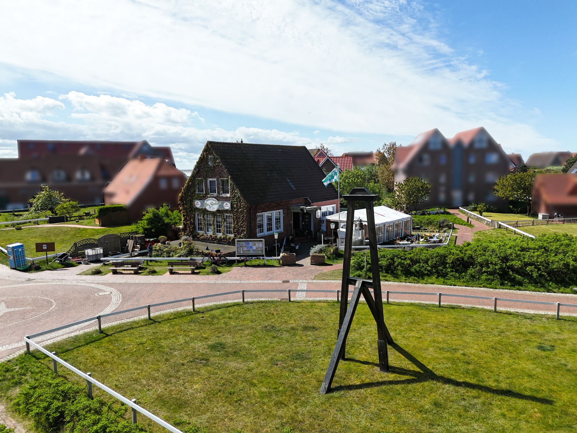Backsteinhaus mit Garten und Terrasse, im Vordergrund eine Holzstruktur auf einer Wiese.
