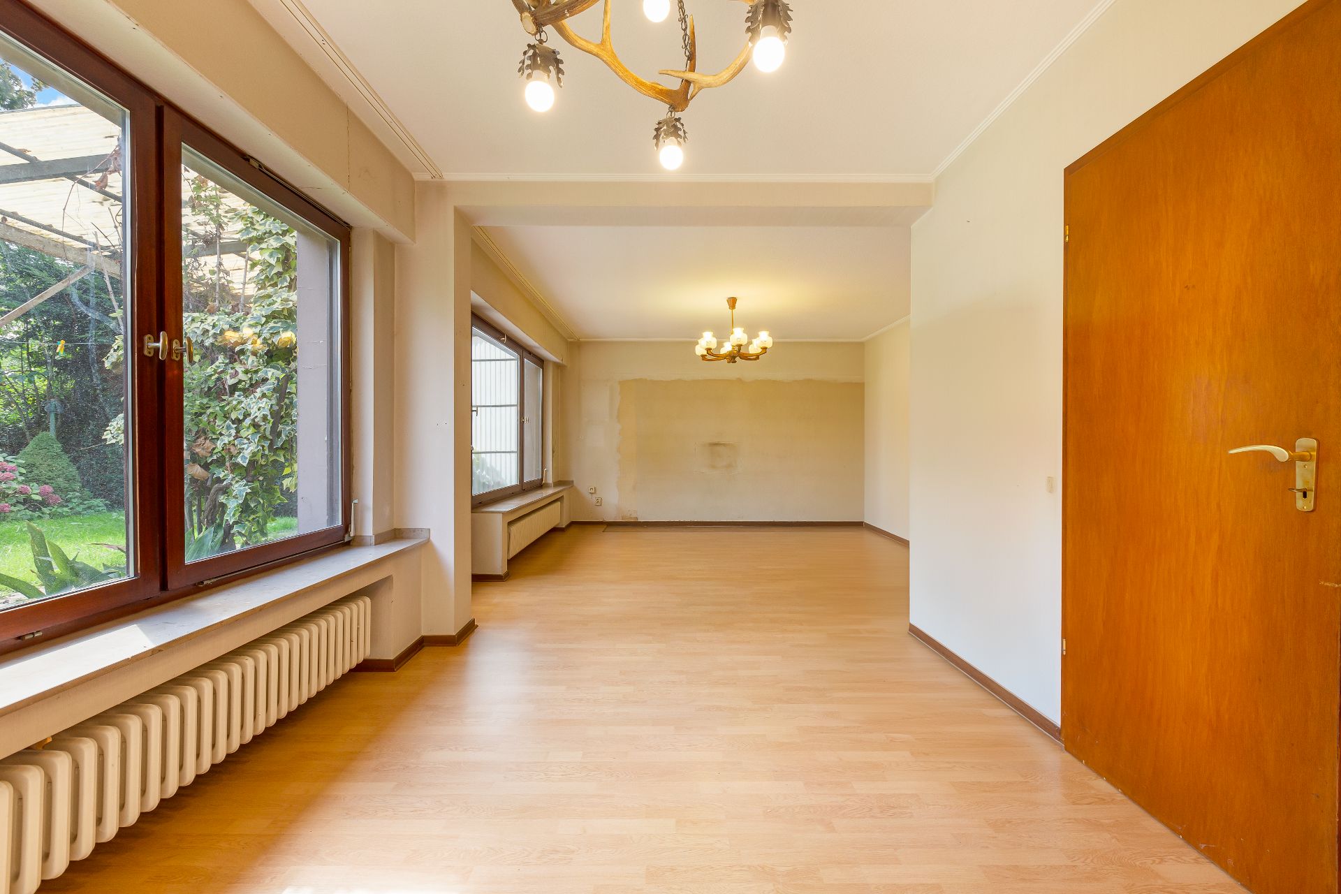 Helles, leeres Wohnzimmer mit Parkettboden, großen Fenstern und zwei Deckenlampen.