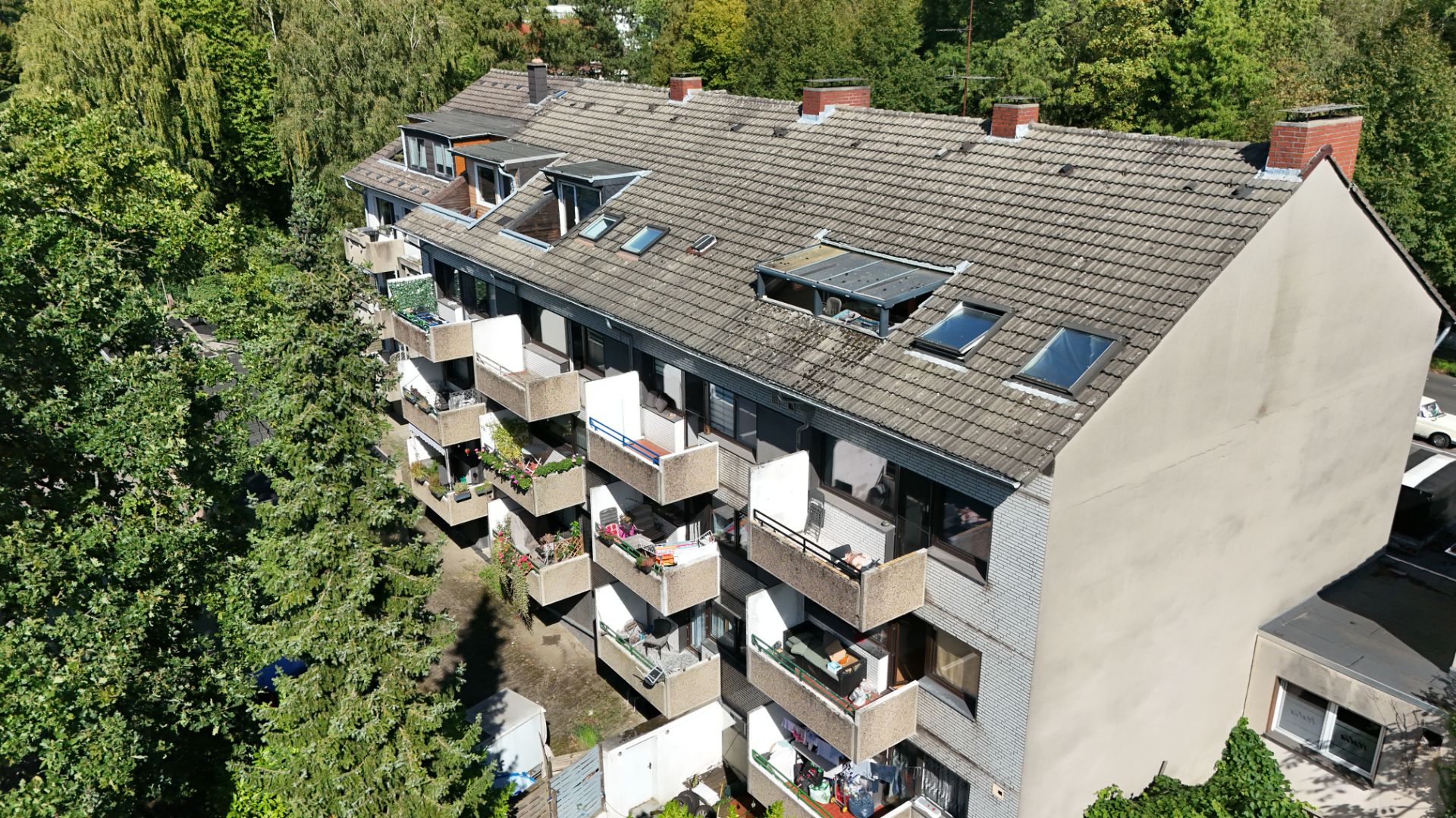 Mehrfamilienhaus mit mehreren Balkonen und begrünten Bäumen im Hintergrund.