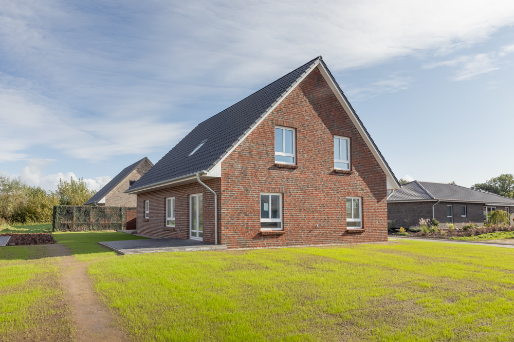 Modernes Einfamilienhaus aus rotem Klinker mit Satteldach im Garten.