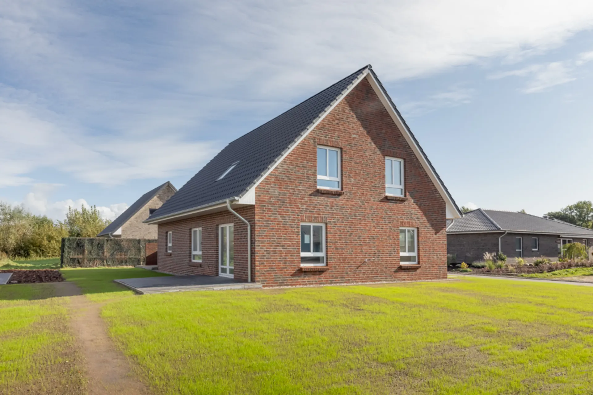 Modernes Einfamilienhaus aus rotem Klinker mit Satteldach im Garten.
