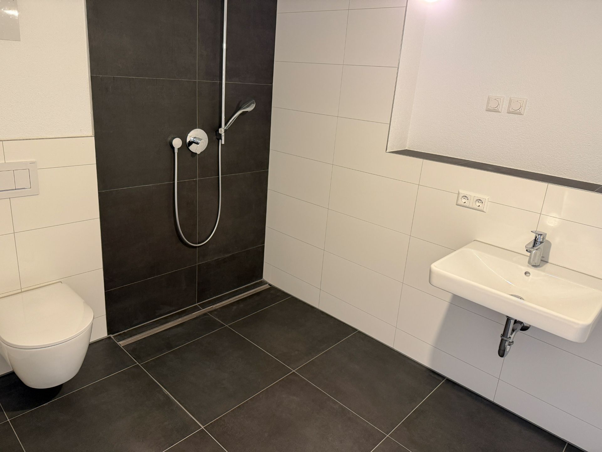 Modernes Badezimmer mit bodengleicher Dusche, Wandtoilette und Waschbecken.