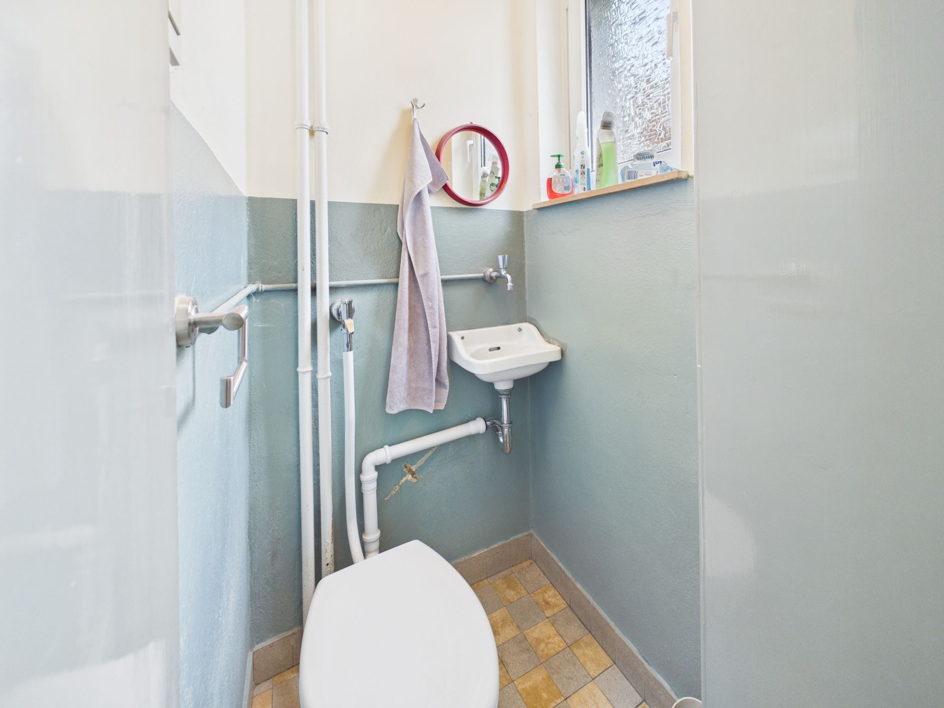 Kleines Badezimmer mit Toilette, kleinem Waschbecken, Spiegel und Fenster.