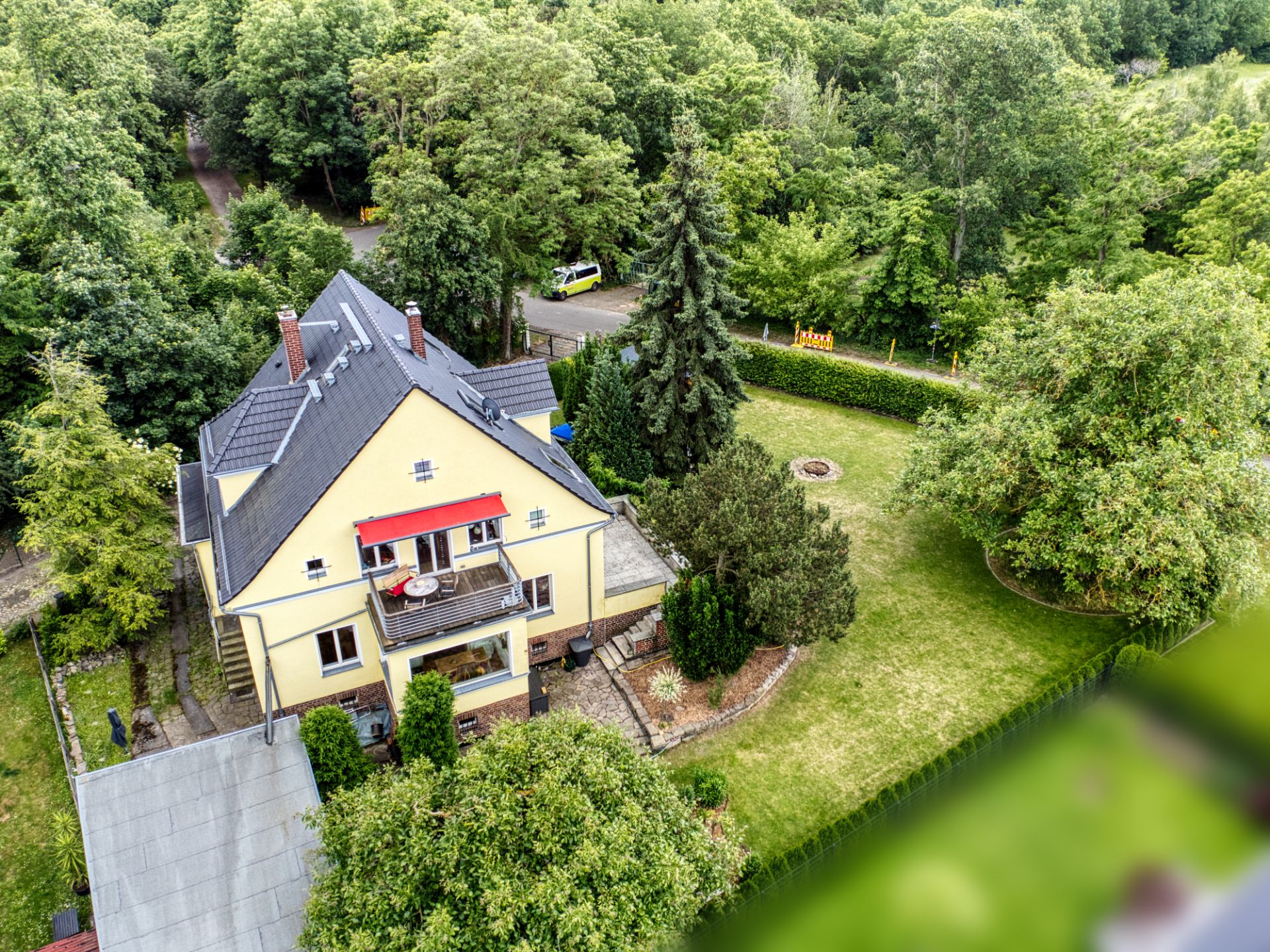 Luftaufnahme eines gelben Wohnhauses mit Balkon und großem Garten, umgeben von Bäumen.