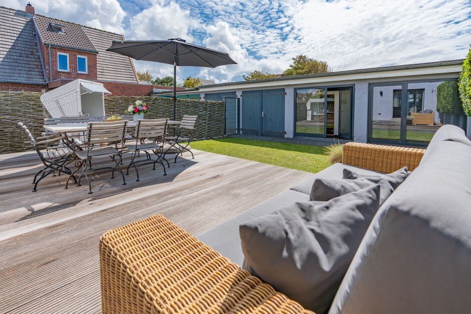 Holzterrasse mit Sitzgruppe, Sofa, Sonnenschirm und Rasenfläche im Garten eines Wohnhauses.