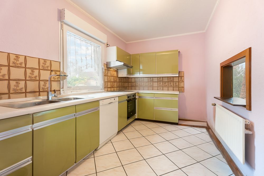 Küche mit grünen Schränken, weißer Arbeitsplatte, Fliesenboden und Fenster.