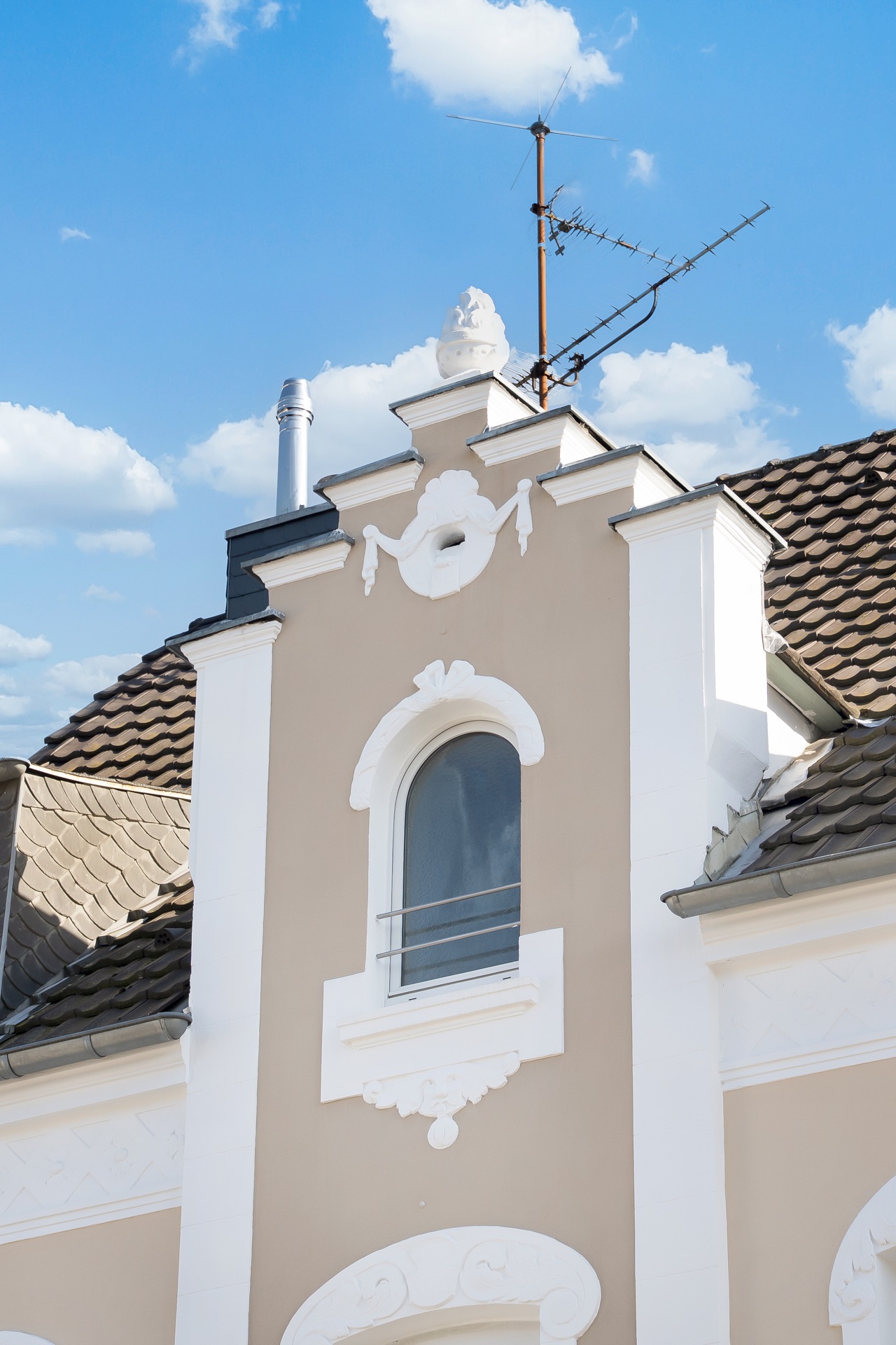 Detailansicht einer Hausfassade mit verziertem Giebel, Fenster und Dach mit Antenne.