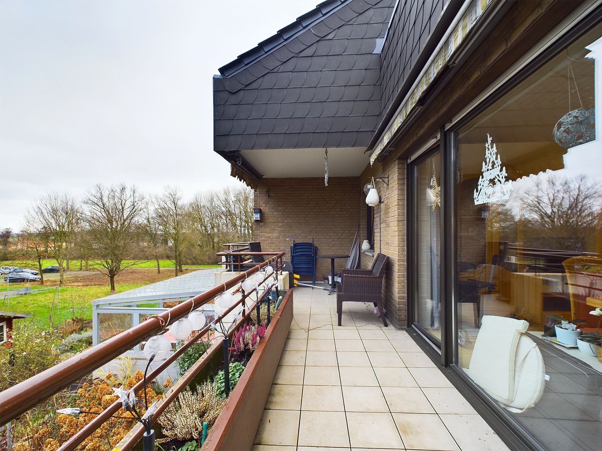 Großer Balkon mit Möbeln, Pflanzen und Blick auf Bäume und Wiese.