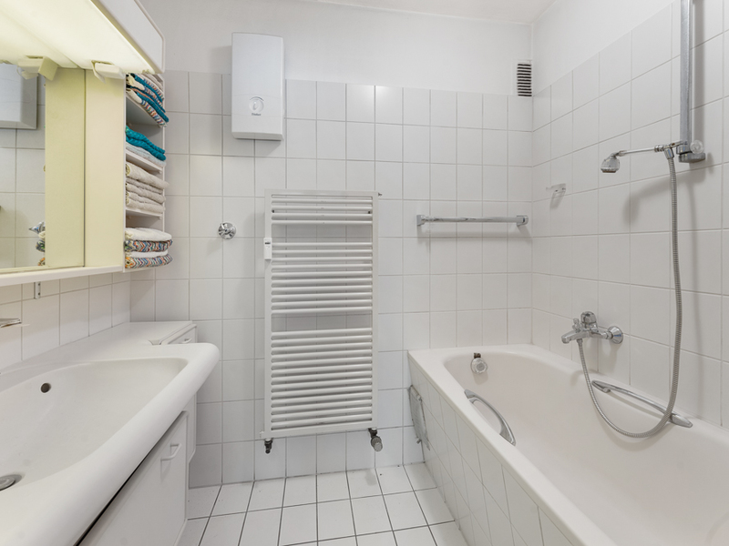 Helles Badezimmer mit Badewanne, Waschbecken, Handtuchheizkörper und weißen Fliesen.