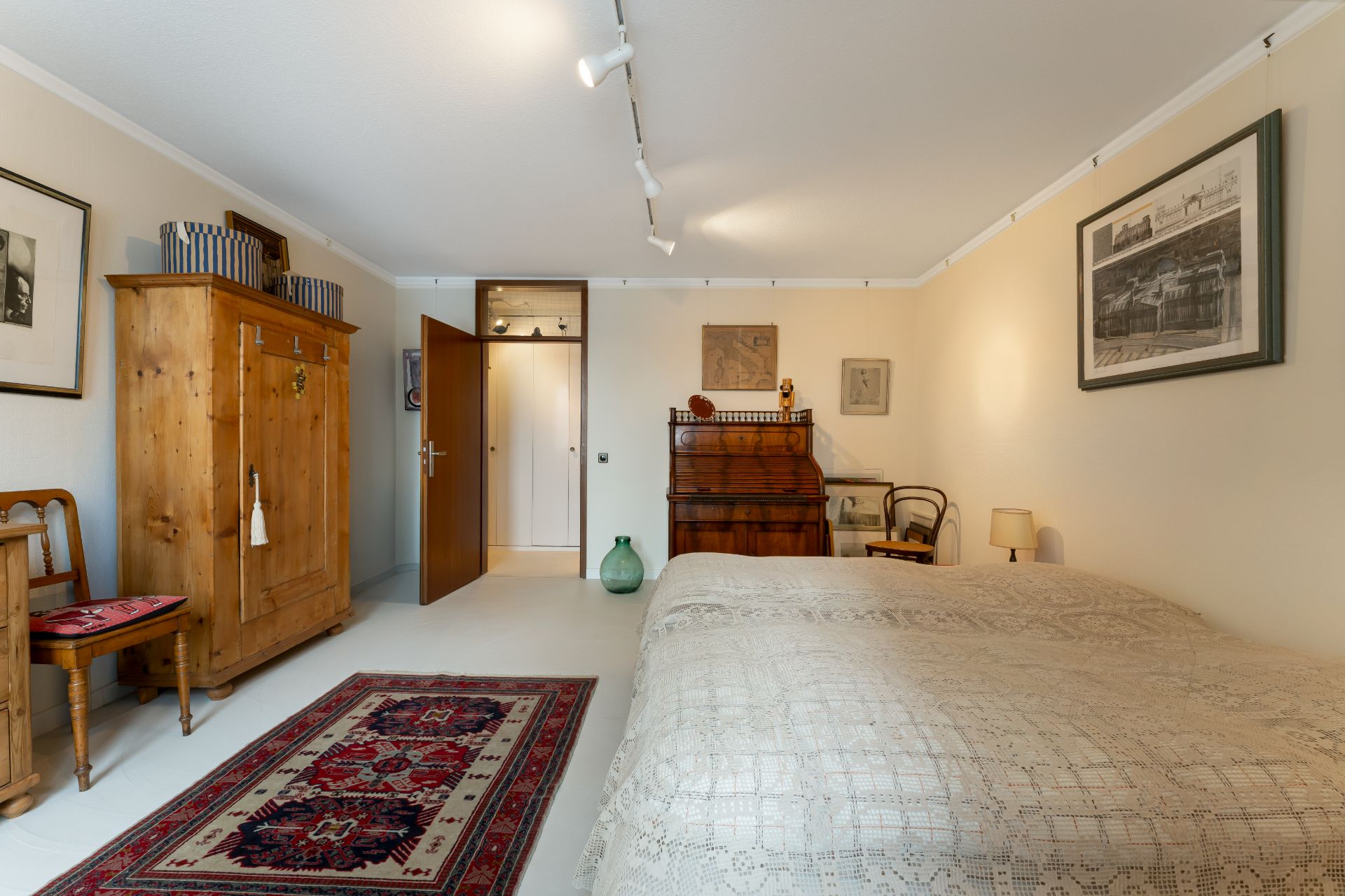 Schlafzimmer mit großem Bett, Holzmöbeln, Teppichen und Bildern an den Wänden.