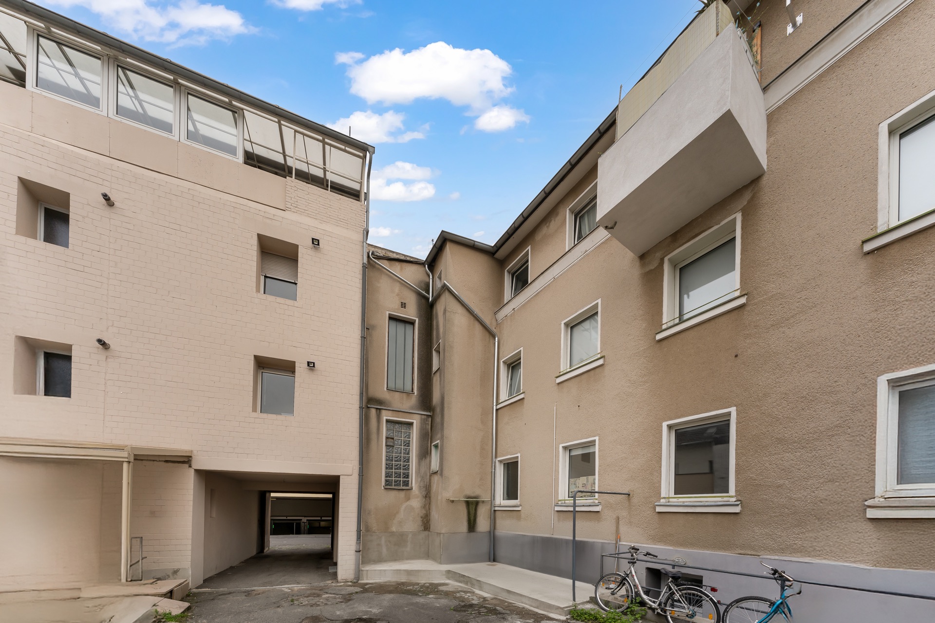 Innenhof eines Wohngebäudes mit mehreren Fenstern, Balkon und zwei Fahrrädern vor der Hauswand.