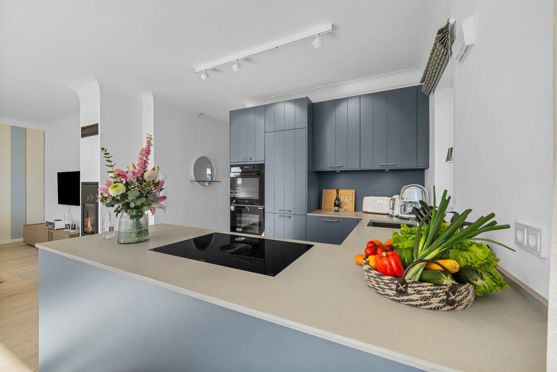 Moderne Küche mit blauen Schränken, Kücheninsel, Blumenstrauß und Korb mit Gemüse.