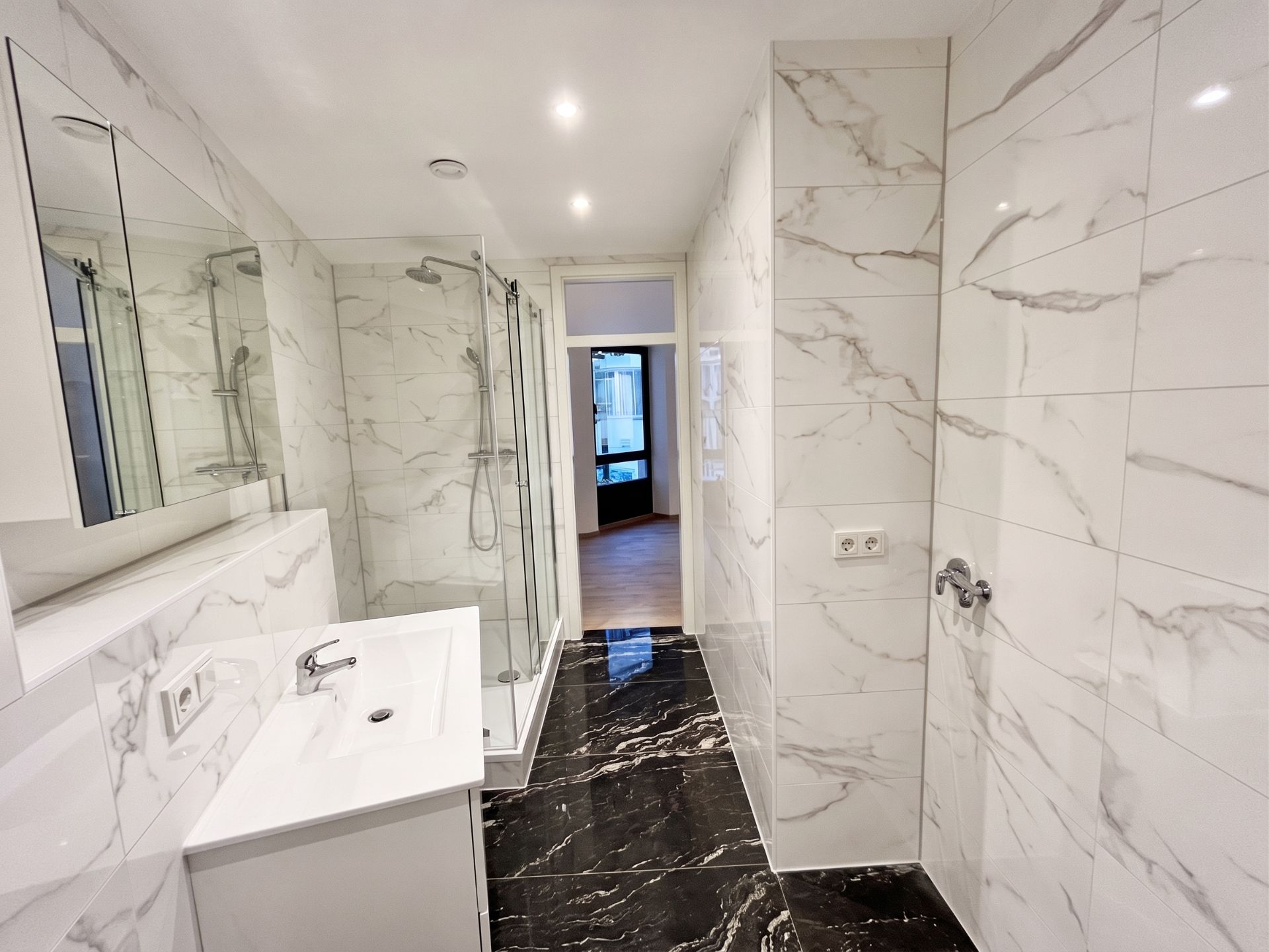 Modernes Badezimmer mit Marmorfliesen, Dusche, Waschbecken und Spiegel.